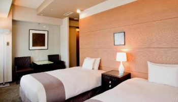 Citadines Central Shinjuku Tokyo: Twin beds in a gay-friendly hotel room. Features bedside table, lamp, seating area, and modern decor.