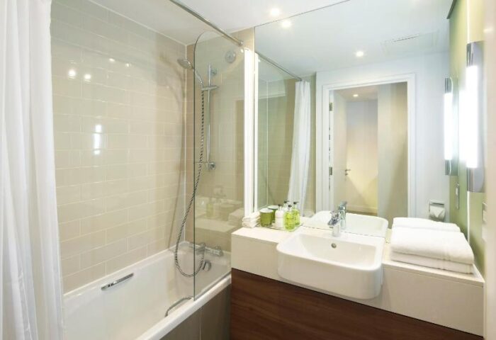 Bathroom at Citadines Holborn-Convent Garden London, a gay-friendly hotel. Features a tub, shower, sink, mirror, and modern design.