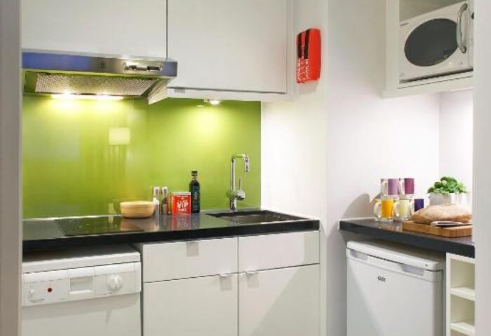 Citadines Holborn-Convent Garden London kitchenette. Modern design with white cabinets, green backsplash, and black countertops. Gay-friendly hotel.