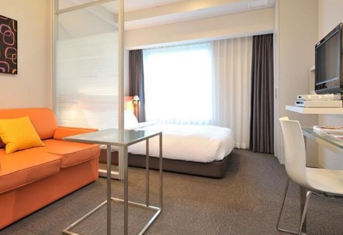 Citadines Shinjuku Hotel room. Gay-friendly hotel with orange sofa, bed, desk, and TV. Modern design for a comfortable stay in Shinjuku, Tokyo.