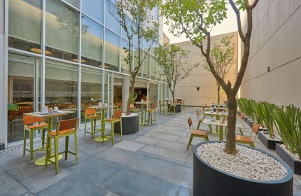 City Express Plus by Marriott Ciudad de Mexico Reforma El Ángel outdoor dining area. Gay-friendly hotel with tables, chairs, and trees in pots. Modern design.