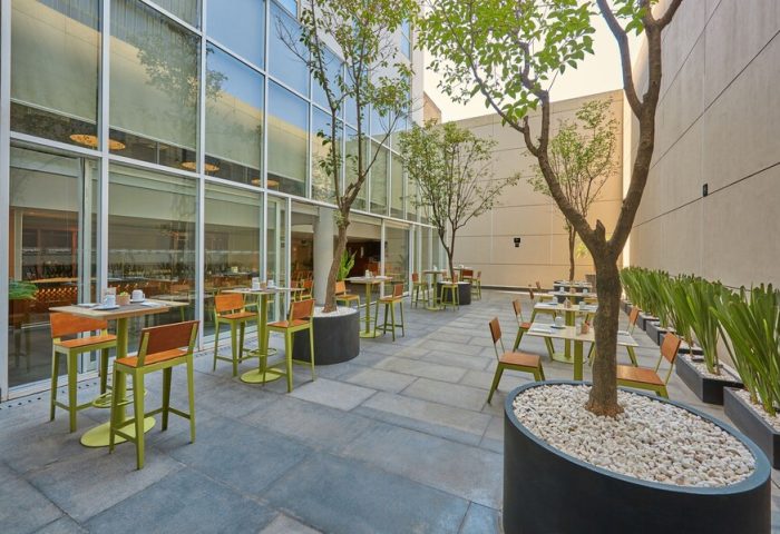 City Express Plus by Marriott Ciudad de Mexico Reforma El Ángel outdoor dining area. Gay-friendly hotel with tables, chairs, and trees in pots. Modern design.
