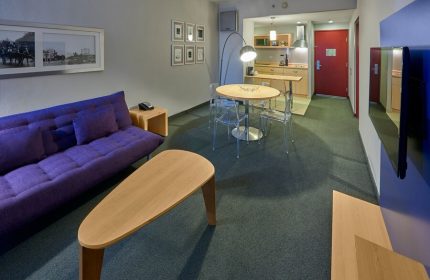 City Express Plus by Marriott Ciudad de Mexico Reforma El Angel room. Gay-friendly hotel with purple couch, table, and kitchenette. Modern design.