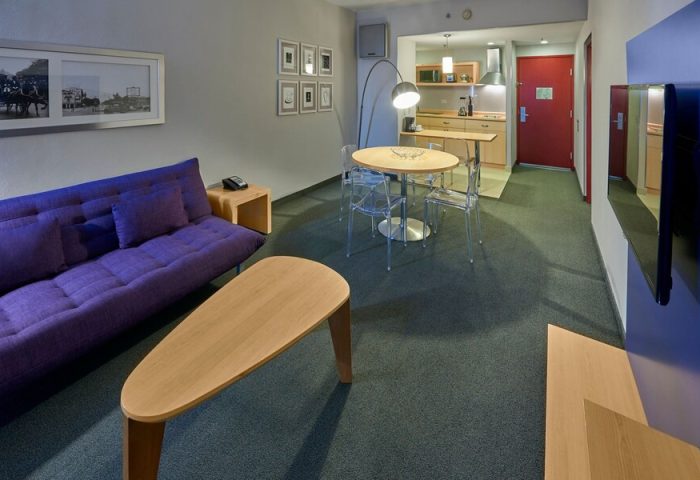 City Express Plus by Marriott Ciudad de Mexico Reforma El Angel room. Gay-friendly hotel with purple couch, table, and kitchenette. Modern design.