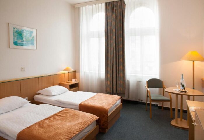 City Hotel Matyas room with twin beds. Gay-friendly hotel with champagne, glasses, and snacks on a round table. Window with curtains.