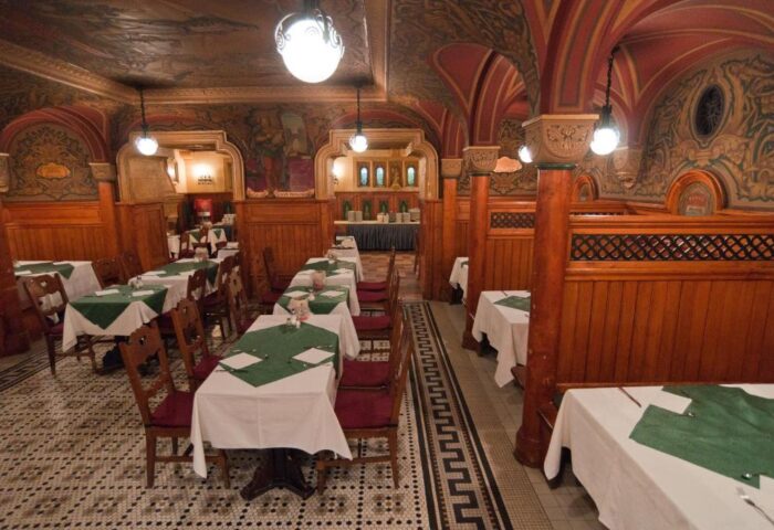 City Hotel Matyas gay-friendly restaurant interior. Tables with green cloths, wood paneling, painted walls, and ornate ceiling.