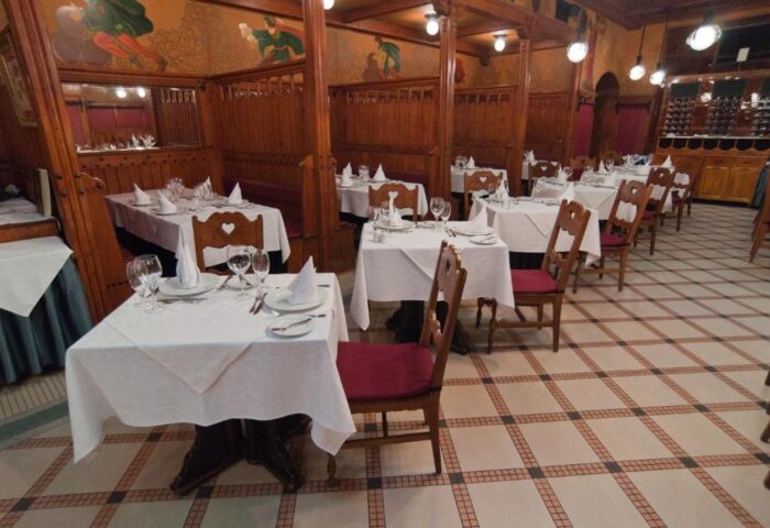 City Hotel Matyas restaurant interior. Tables with white tablecloths, wooden chairs, and booths. Gay-friendly hotel dining in Budapest.
