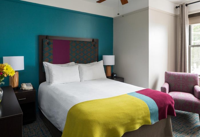City Suites Chicago gay-friendly hotel room. Queen bed with colorful blanket, headboard, & accent wall. Chair by window. LGBTQ travel.