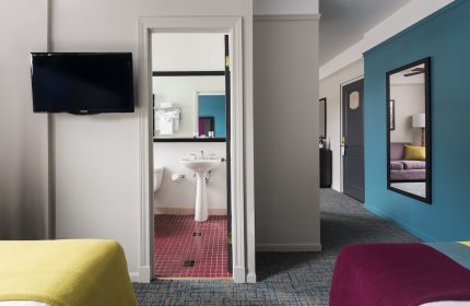 City Suites Chicago gay-friendly hotel room. Bathroom view with pedestal sink, red tile. Blue wall, mirror, and purple couch in the suite.