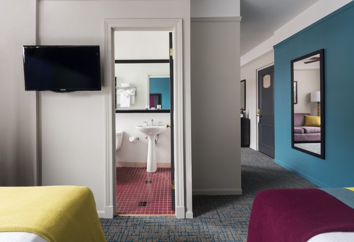 City Suites Chicago gay-friendly hotel room. Bathroom view with pedestal sink, red tile. Blue wall, mirror, and purple couch in the suite.
