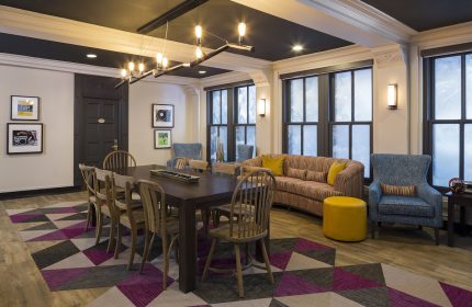 City Suites Chicago gay-friendly hotel lounge area. Long table, chairs, sofa, and armchairs create a welcoming space. Geometric rug adds flair.