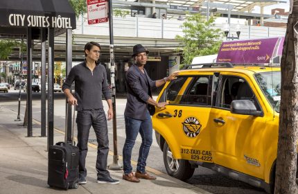 Gay-Friendly Hotel City Suites Chicago: Two men with luggage by a Yellow Cab taxi. Belmont train station in background. Chicago travel.