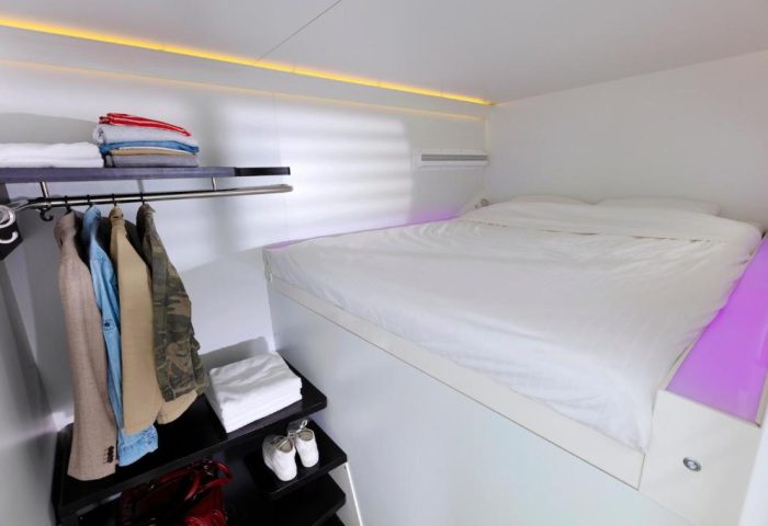 CityHub Amsterdam gay-friendly hotel room. Minimalist design, elevated bed, closet with clothes, shelves with towels and shoes. Modern, clean.