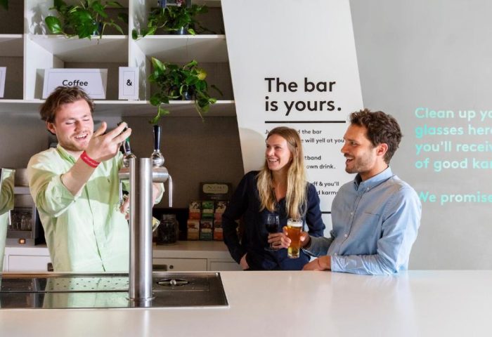 CityHub Amsterdam's bar area, a gay-friendly hotel. Staff member serving drinks to guests. The bar is yours. Modern, social hotel.