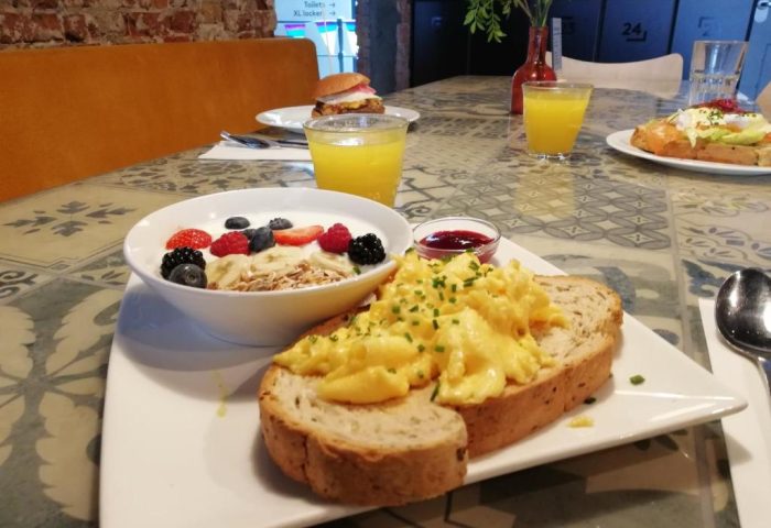 Breakfast at CityHub Amsterdam, a gay-friendly hotel: yogurt with berries, scrambled eggs on toast, juice, and a burger.