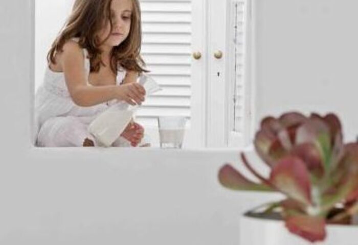 Child pours milk in a Cliff Side Suites gay-friendly hotel room. White decor, shutters, and potted plant create a serene atmosphere.