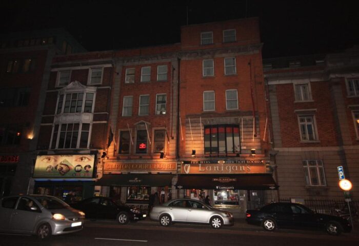 Night view of Clifton Court Hotel, a gay-friendly hotel in Dublin. The hotel's facade is visible, with cars parked in front.