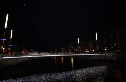 Night view near Clifton Court Hotel, a gay-friendly hotel. Bridge over water with lights reflecting. Gay travel in Dublin.