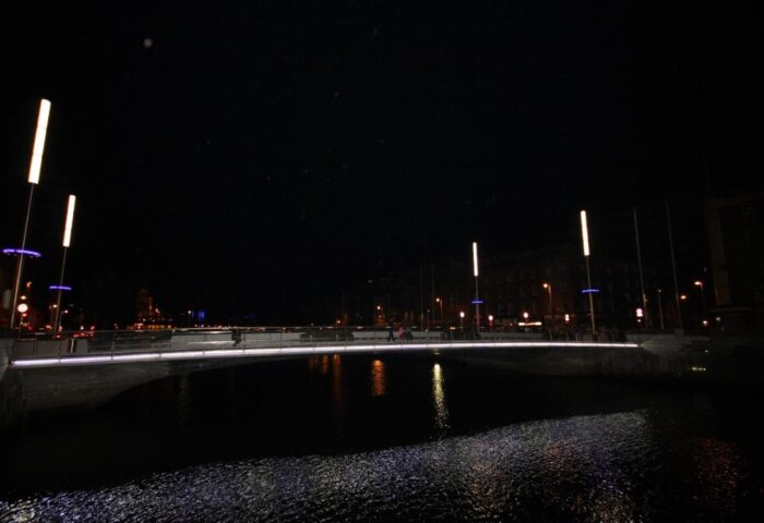 Night view near Clifton Court Hotel, a gay-friendly hotel. Bridge over water with lights reflecting. Gay travel in Dublin.