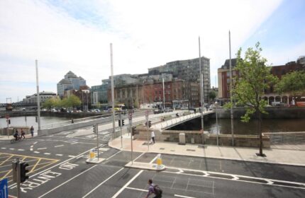 Dublin street view from Clifton Court Hotel, a gay-friendly hotel. A cyclist rides on the road near the river and bridge.