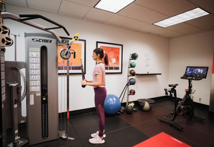 Gym at Club Quarters Hotel Central Loop, a gay-friendly hotel. Woman using Cybex weight machine. Exercise equipment and medicine balls visible.