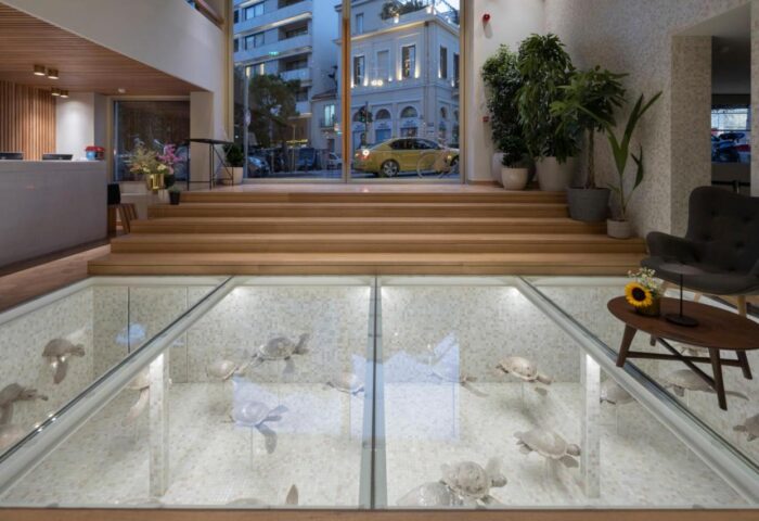 Coco-mat Athens BC gay-friendly hotel lobby. Glass floor reveals turtle sculptures. Modern design, inviting atmosphere for gay travelers.