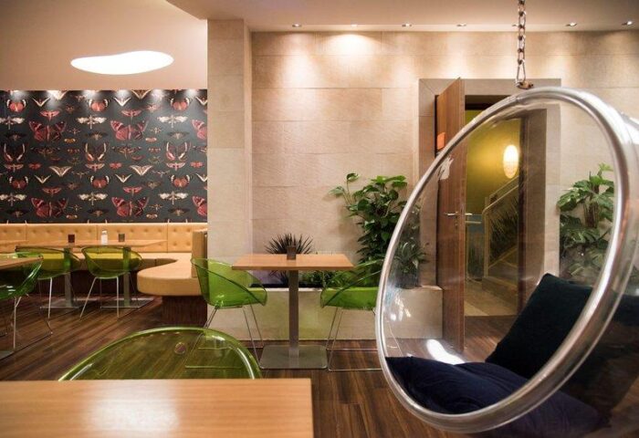 Cocoon Sendlinger Tor's interior. Gay-friendly hotel with stylish design: butterfly wallpaper, green chairs, hanging bubble chair, plants.