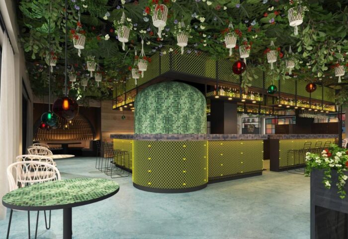 Interior of Cocoon Sendlinger Tor, a gay-friendly hotel. Lush greenery hangs above a modern bar area with unique design elements.