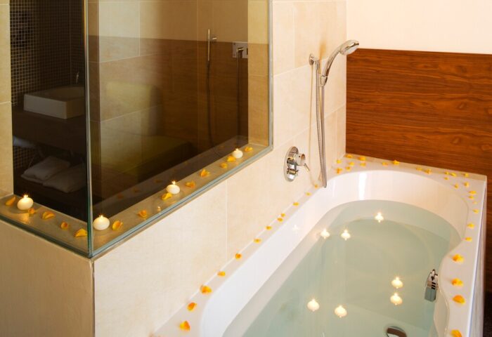 Cocoon Sendlinger Tor gay-friendly hotel bathroom. Bathtub with water, candles, and flower petals. Shower and sink visible. Relaxing spa vibe.