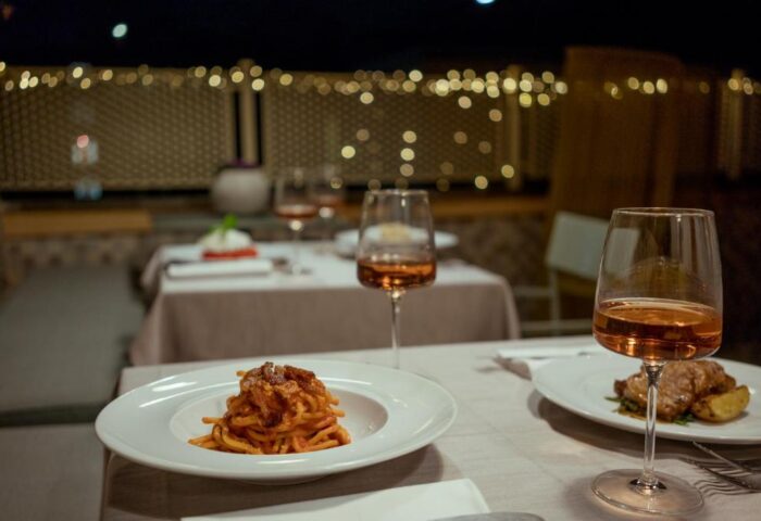 Fine dining at Condominio Monti Boutique Hotel, a gay-friendly hotel. Pasta dish and wine glasses on a beautifully set table. Romantic ambiance.