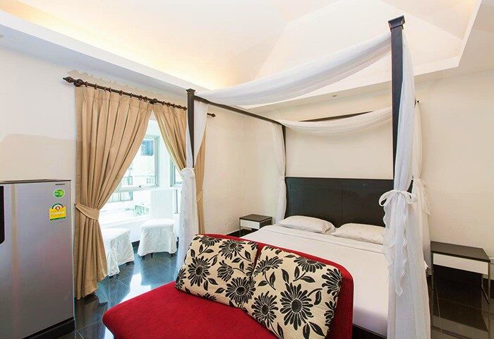 Connect Guesthouse gay-friendly hotel room. Canopy bed, red chaise lounge, and balcony. Modern design for gay men's travel.