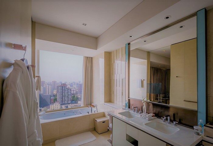 Bathroom at Conrad Beijing, gay-friendly hotel. Bathtub by window with city view. Double sinks, mirror, robes. Luxury travel for gay men.
