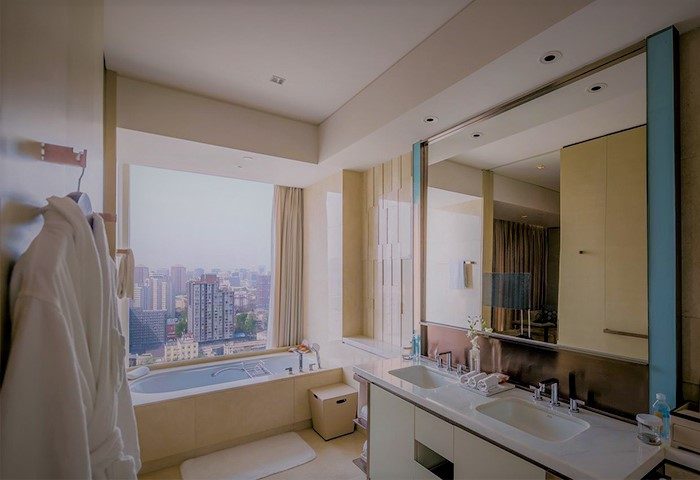 Bathroom at Conrad Beijing, gay-friendly hotel. Bathtub by window with city view. Double sinks, mirror, robes. Luxury travel for gay men.
