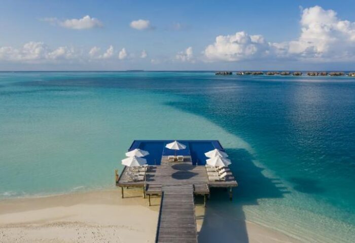 Conrad Maldives Rangali Island Resort: Gay-friendly hotel with overwater bungalows, pool, umbrellas, and sunbeds on a wooden deck. Tropical paradise.