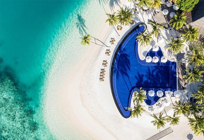 Aerial view of Conrad Maldives Rangali Island Resort. Blue pool, white sand beach, palm trees. Gay-friendly hotel. Maldives vacation.