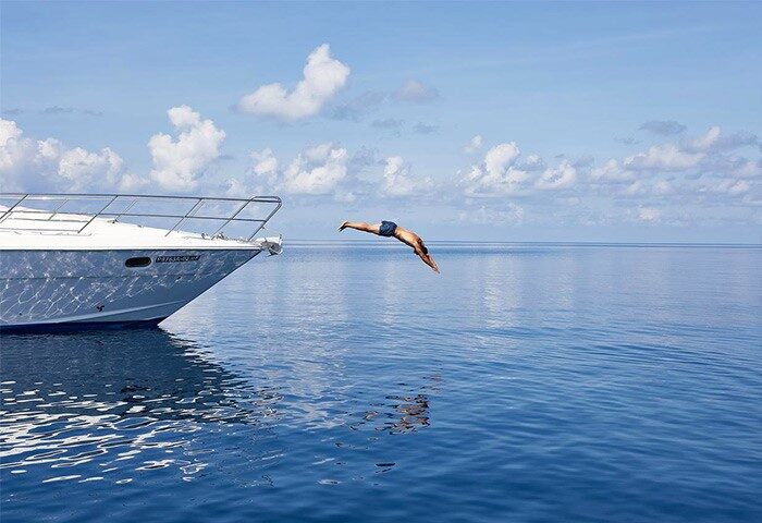 Man diving from boat at Conrad Maldives Rangali Island Resort. Gay-friendly hotel offers luxury travel for gay men. Blue water, sky, and boat.