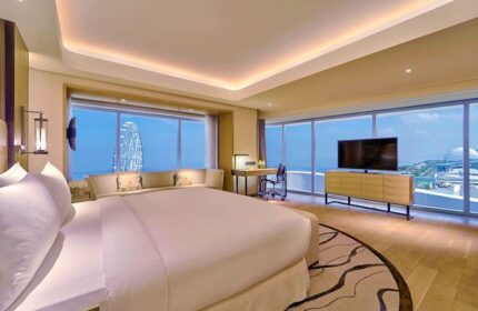 Conrad Manila gay-friendly hotel room. Spacious suite with a large bed, desk, and floor-to-ceiling windows offering ocean views and a Ferris wheel.