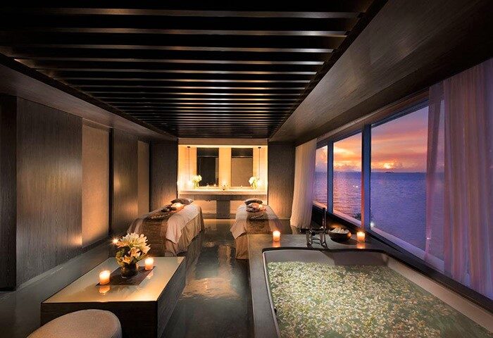 Gay-Friendly Hotel Conrad Manila spa room. Two massage beds, a flower-filled tub, and ocean sunset views. Relaxing travel experience.