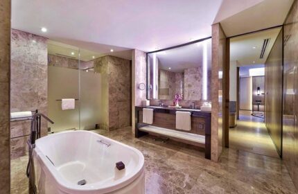 Bathroom at Gay-Friendly Hotel Conrad Manila. Features a tub, double sink vanity, marble walls and floors, and a glass-enclosed shower.
