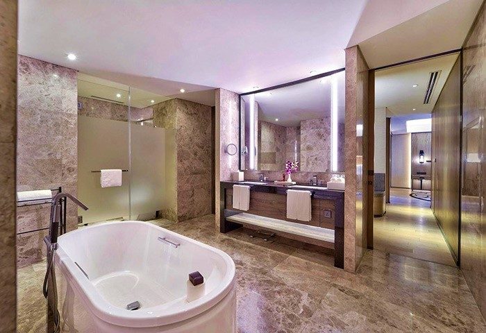 Bathroom at Gay-Friendly Hotel Conrad Manila. Features a tub, double sink vanity, marble walls and floors, and a glass-enclosed shower.