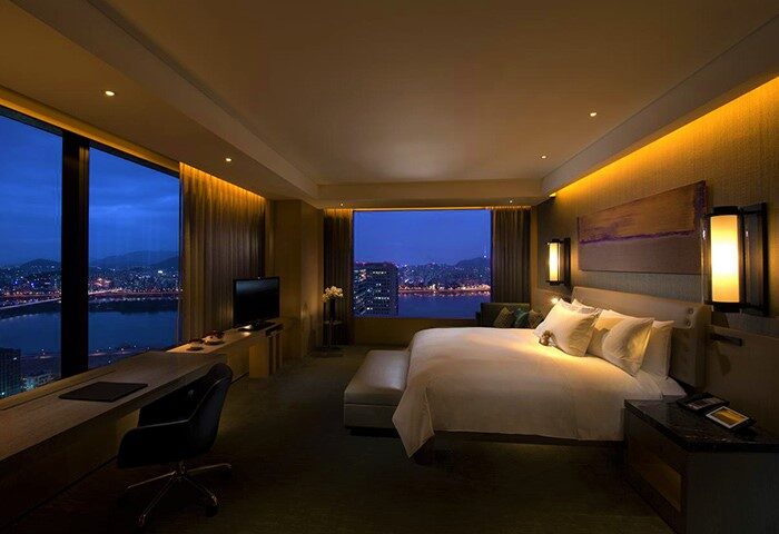 Conrad Seoul hotel room at night. Gay-friendly hotel with a view of the city skyline and river. Luxurious bed, desk, and modern design.