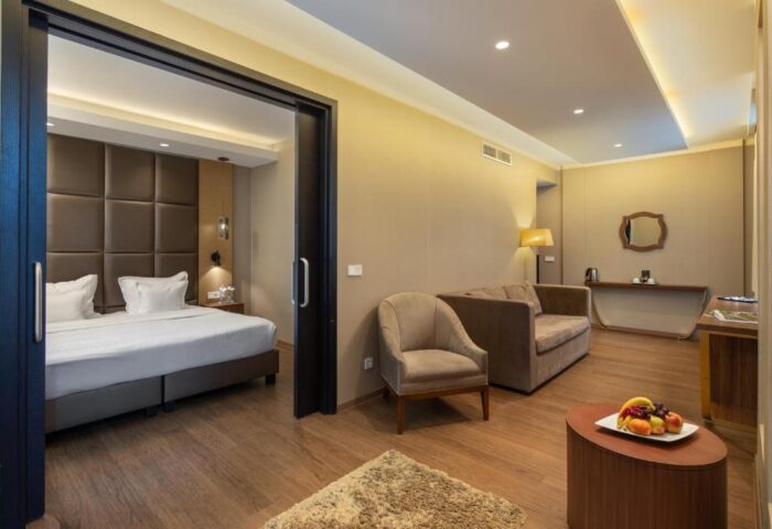 Continental Hotel: Luxurious suite with a bed, sofa, chair, and fruit plate. Gay-friendly hotel room offers comfort and style for discerning travelers.