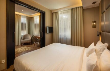 Continental Hotel room. Gay-friendly hotel featuring a king-size bed with white linens, curtains, and a sitting area with a desk and chair.