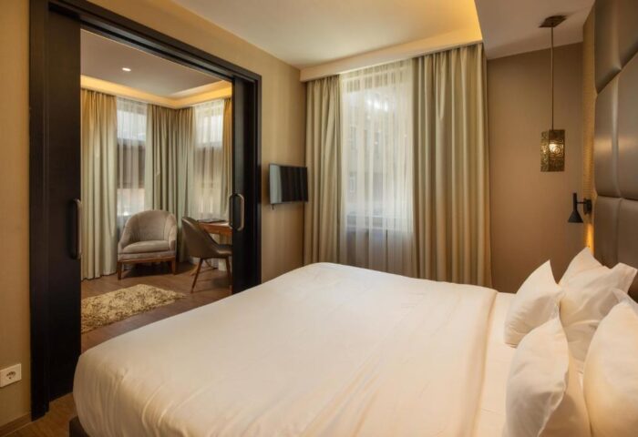 Continental Hotel room. Gay-friendly hotel featuring a king-size bed with white linens, curtains, and a sitting area with a desk and chair.