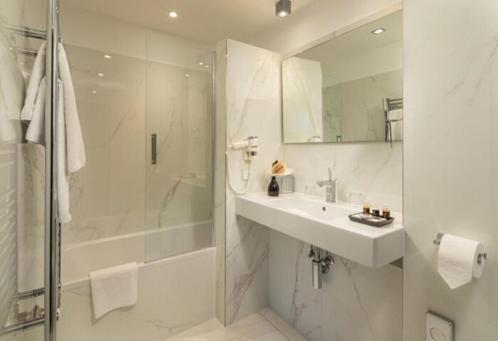 Bathroom at the Gay-Friendly Continental Hotel. Features a modern sink, mirror, shower with glass door, and marble accents. Upscale amenities.