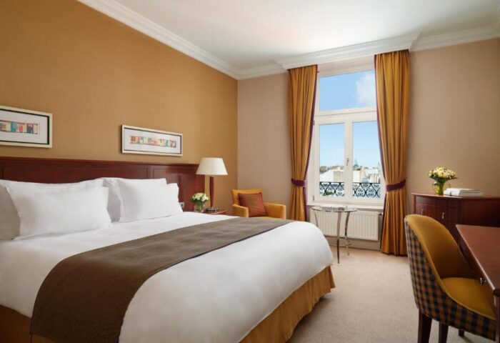 Corinthia Hotel Budapest bedroom. Gay-friendly, pet-friendly hotel room with a bed, window, desk, and chair. Comfortable stay for gay travelers.