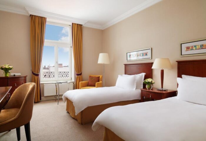 Corinthia Hotel Budapest, gay-friendly, pet-friendly room. Twin beds, desk, chair, and window with city view. Comfortable, welcoming space.