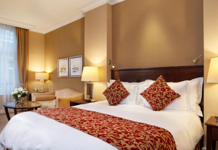 Corinthia Hotel Budapest room. Gay-friendly, pet-friendly hotel with a king-size bed, red floral accents, and a sitting area. Luxury travel.