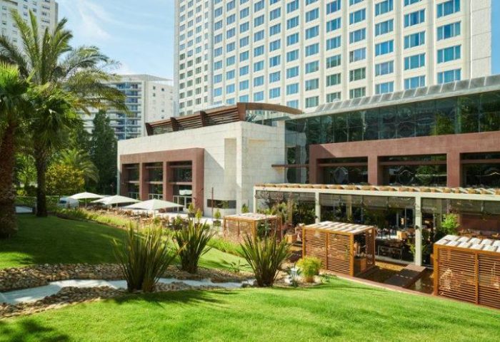 Exterior view of Corinthia Hotel Lisbon, a gay-friendly, pet-friendly hotel. Lush green lawn, palm trees, and modern architecture.