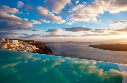 Cosmopolitan Suites, a gay-friendly hotel. Infinity pool overlooking Santorini's caldera, Aegean Sea, and whitewashed buildings on the cliff.